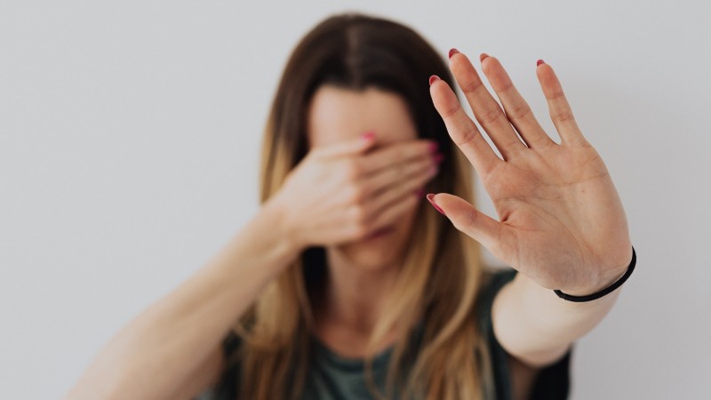 foto de uma mulher tapando os olhos com uma mão e fazendo um sinal de "pare" com a outra mão