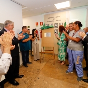 foto geral do descerramento da placa em homenagem a Mauro Marques da Silva. A placa está ao fundo e os participantes do evento formam um "U" e aplaudem