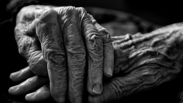foto de duas mãos idosas, uma por cima da outra, em preto e branco