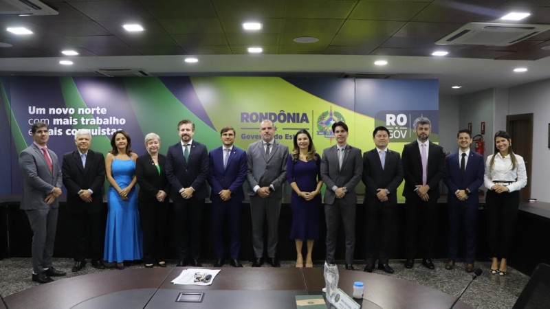 Na foto, há 13 pessoas, homens e mulheres, em frente a um backdrop do Estado de Rondônia