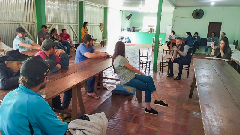 imagem do salão da igreja, com vários moradores sentados e o defensor público conversando com eles