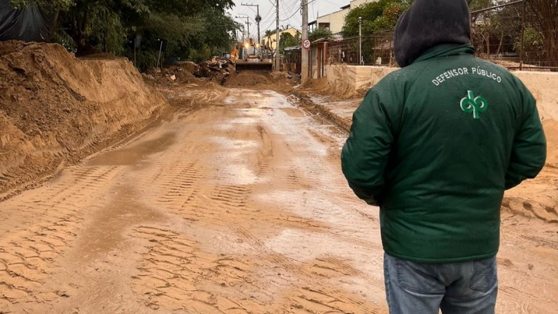 Foto de defensor público, de costas, olhando para rua enlameada, nas ilhas de porto alegre