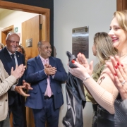 5 pessoas aparecem na foto fazendo o descerramento da placa de inauguração da 2ª Delegacia Especializada de Atendimento à Mulher.