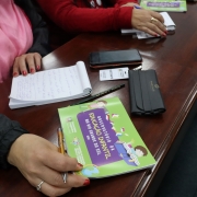 Uma pessoa, cujo rosto está fora do enquadramento da foto, manuseia um bloco de notas e um papel escrito "observatório da educação infantil do rio grande do sul", em cima de uma mesa. 