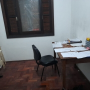 Sala com janela, cadeira e mesa com papéis em cima.