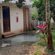 Casa com gramado e árvores na frente. Na entrada, em frente à porta, há uma poça d'água no chão.