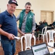 imagem de um servidor sorrindo e de frente para a foto, ao lado de um morador que também está de frente e olhando para o servidor que vai atendê-lo, que está de costas para a foto