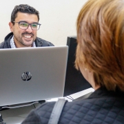 imagem de um defensor, de frente para a foto, sorrindo e olhando para uma senhora que é atendida e está de costas para a foto