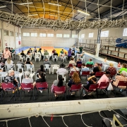 foto do espaço onde ocorreu o mutirão, ela foi tirada de cima, e no espaço entre a trave de uma goleira e a rede do ginásio, está o cenário com muitas cadeiras e mesas e pessoas sendo atendidas