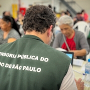 foto de um defensor atendendo, de costas para a câmera, com um colete da defensoria pública de são paulo