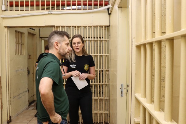 Na foto, há um homem e uma mulher, estão conversando e observando uma cela. 