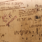 Na imagem, vê-se a porta de uma cela com diversas coisas escritas, entre elas "respira a liberdade", "tenha fé em deus"