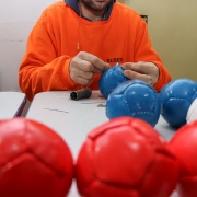 Na foto, há um homem costurando uma pequena bola 