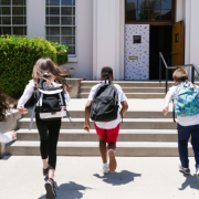 5 crianças correndo em direção à entrada de uma escola.