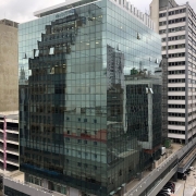 Foto do prédio da Defensoria Pública a meia altura do prédio, possibilitando ver os prédios ao lado, a rua e o Rio Guaíba ao fundo.