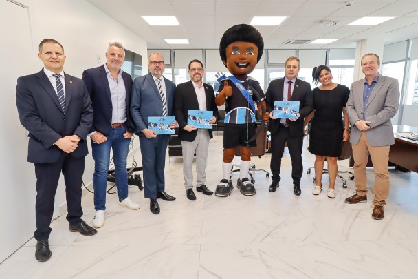 Na foto, há seis homens, uma mulher e o mascote do Grêmio, todos em pé, sorrindo para foto