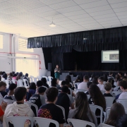 Foto geral do evento, auditório com crianças e a defensora ao fundo