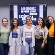 7 mulheres, uma ao lado da outra, posam para a foto. Atrás delas, uma tela em que se pode ler “Corredoras de Porto Alegre contra o Assédio e Importunação Sexual”.