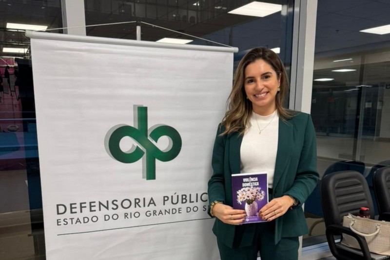 Foto geral da defensora segurando a cartilha sobre conscientização de violência doméstica da Defensoria Pública do Estado do Rio Grande do Sul