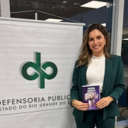 Foto geral da defensora segurando a cartilha sobre conscientização de violência doméstica da Defensoria Pública do Estado do Rio Grande do Sul