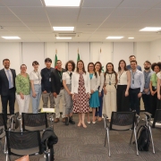 19 pessoas em uma sala, todas de pé, uma do lado da outra, posando para foto.