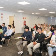 Foto de plateia dentro de sala com várias pessoas sentadas.