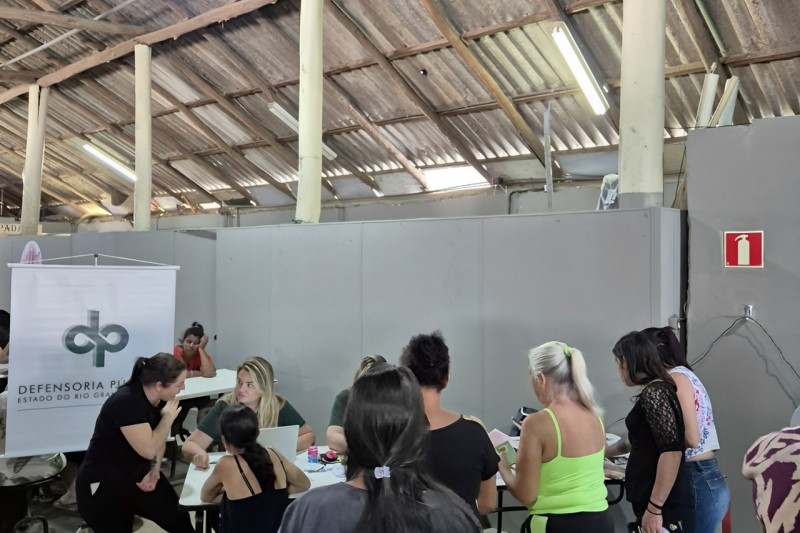 Mesa de atendimento para mulheres. É possível ver a servidora em frente ao banner da Defensoria. 