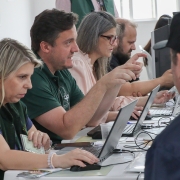 Uma fileira de 2 homens e 2 mulheres sentadas a mesas mexendo em computadores.