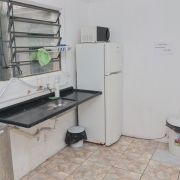 Espaço de cozinha com janela, pia, bebedouro, geladeira, microondas e lixeira.