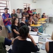 Uma sala escolar com pessoas de pé e sentadas em carteiras.