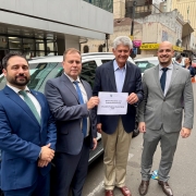 4 homens em frente a um carro na rua, todos de pé e um do lado do outro, posando para a foto. Os 2 do meio seguram um papel escrito "veículo recebido com emenda parlamentar" e "deputado federal afonso motta - PDT"