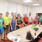 Cerca de 15 pessoas de pé em uma sala ao lado de uma mesa redonda, posando para a foto 